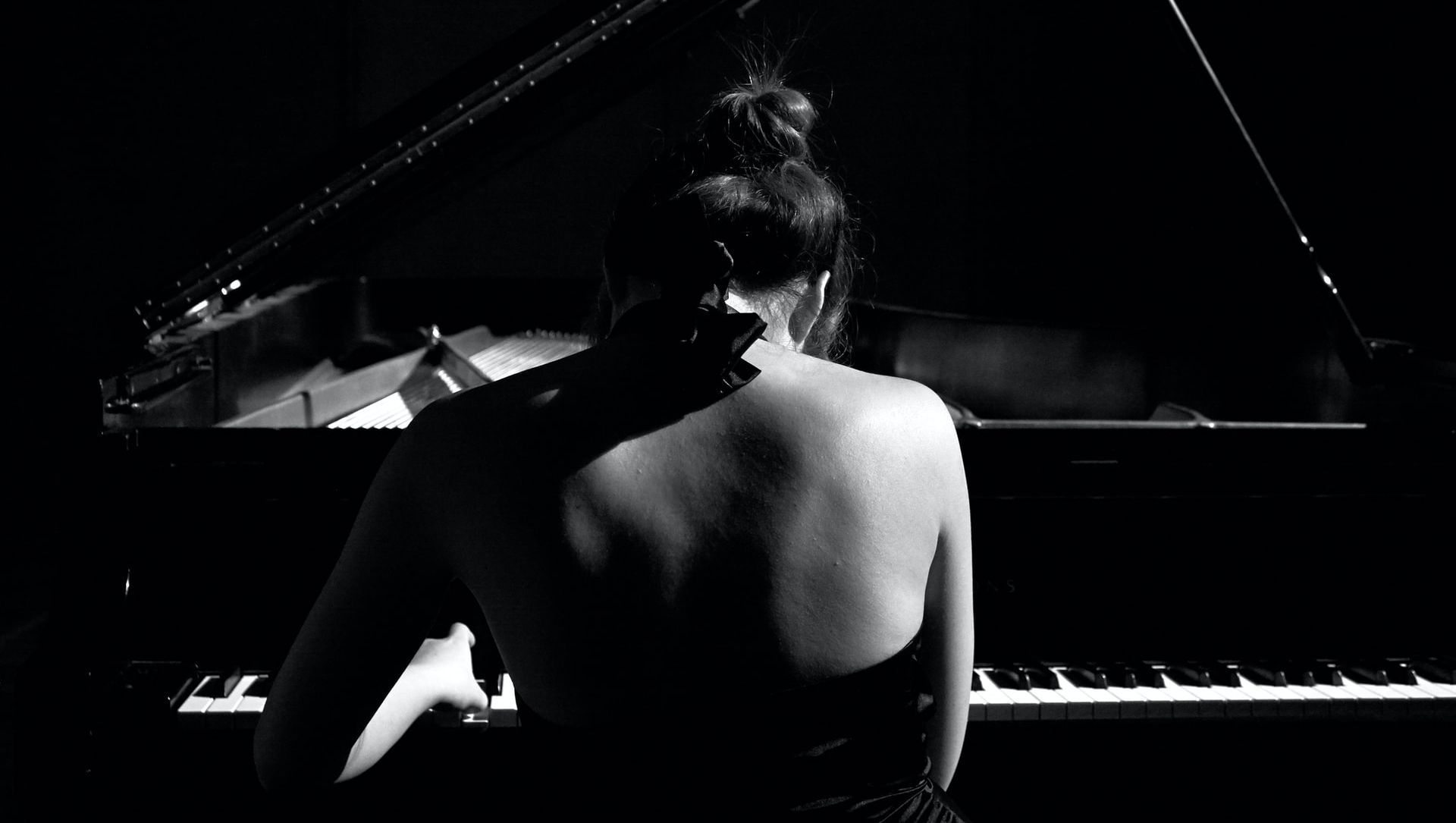 Kvinna i svartvitt som sitter och spelar piano